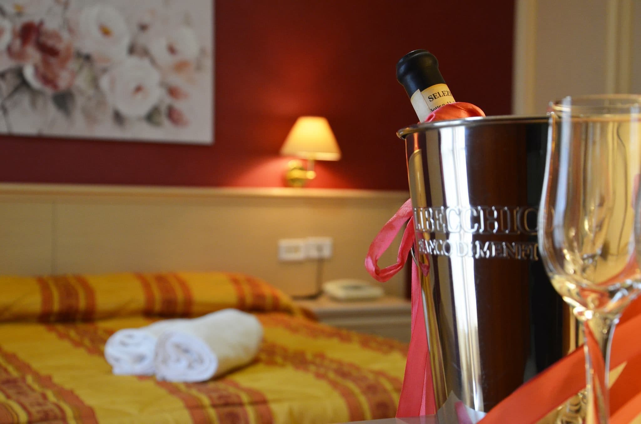 Una habitación de hotel con una cama, una botella de champán en un cubo plateado y una copa de champán.