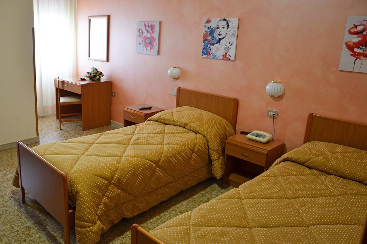A room with two beds, a desk, a chair, and artwork on the walls.