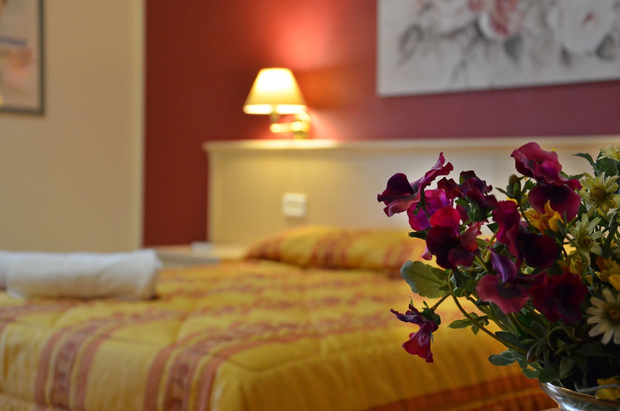 Una habitación de hotel con cama, lámpara de noche y un jarrón de flores.