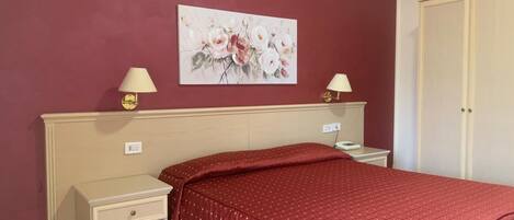 A bedroom with a bed, two bedside tables, a nightstand, a wall-mounted lamp, and a door.