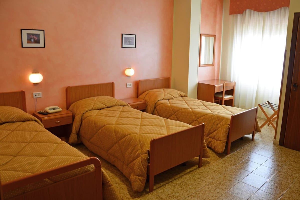 A hotel room with three single beds, a desk, a chair, and a mirror.