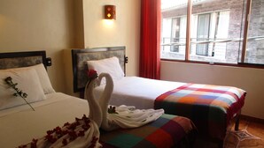 Zwei Betten mit weißen Laken, eine bunte Decke auf einem Bett und eine Rose auf den Kissen.
