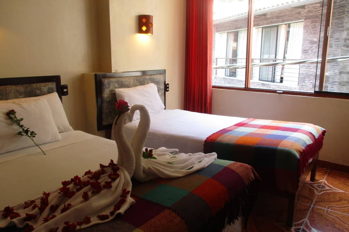 Dos camas con sábanas blancas, una con una manta colorida y una rosa sobre los almohadones.