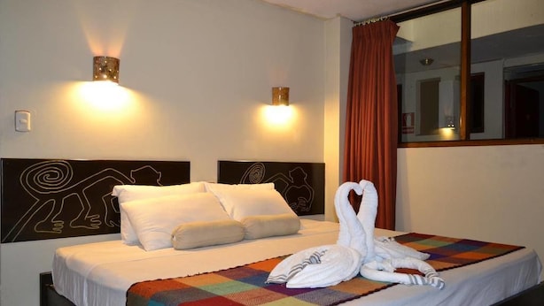 Ein Hotelzimmer mit einem Bett, zwei Wandleuchten, einem Fenster mit Vorhängen und einer farbenfrohen Steudecke.
