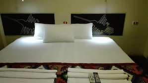 Ein ordentlich bezogenes Bett mit weißen Laken, einer bunten Decke, einer Fernbedienung und einem Handtuch.