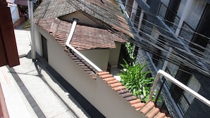 Ein schmaler, erhöhter Balkon mit Ziegeldach, umgeben von dichter Bebauung und Freileitungen.