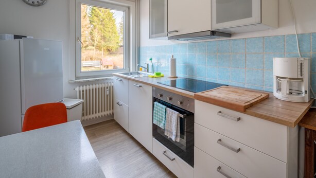 Una cocina moderna con ventana, armarios blancos, horno empotrado y cafetera.