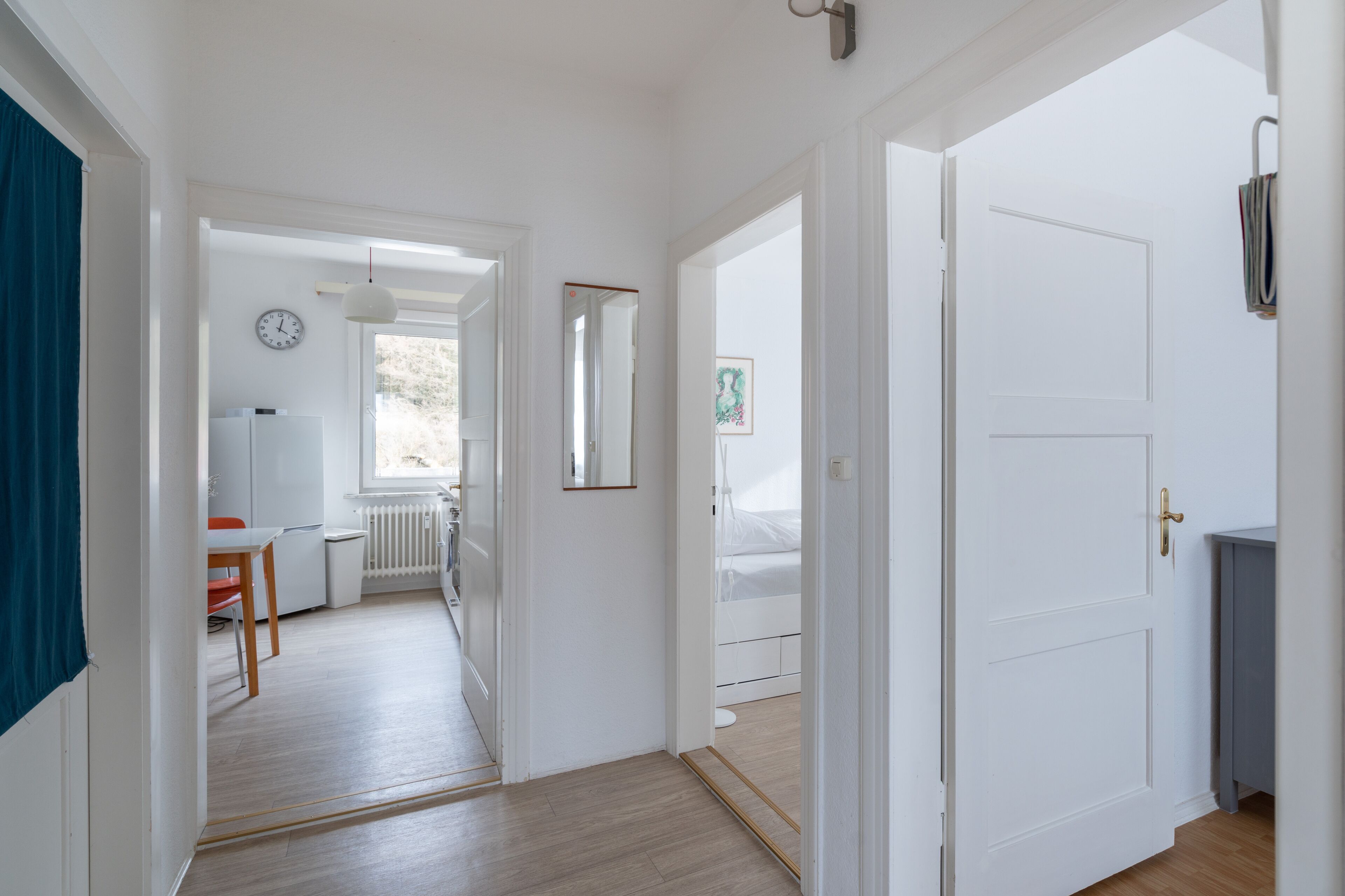 Ein Flur mit einer weißen Tür, einem Heizkörper, einer Uhr und einem Fenster.