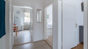 Un pasillo con una puerta blanca, un radiador, un reloj y una ventana.