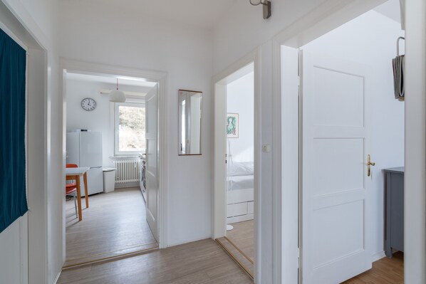 A hallway with a white door, a radiator, a clock, and a window.
