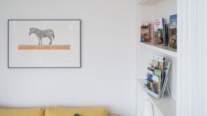 Pared blanca con una ilustración enmarcadas de una cebra y un estante blanco con folletos de viajes.