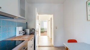 Una cocina con microondas, cafetera y tabla de cortar de madera. Hay una mesa de comedor con una silla roja y una pared blanca con un cuadro enmarcado.