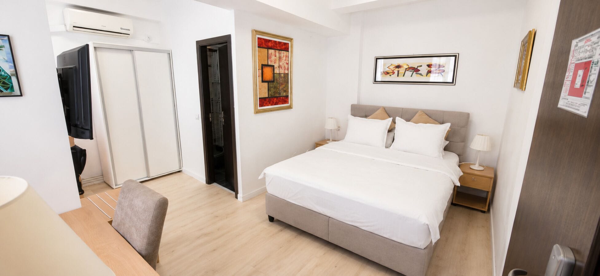Een hotelkamer met een bed, nachtkastjes, een bureau, een stoel en kunstwerken aan de wanden.