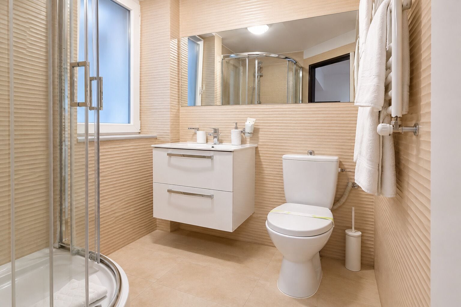 Une salle de bain moderne avec une douche à parois de verre, des toilettes blanches et un meuble-lavabo avec des tiroirs.