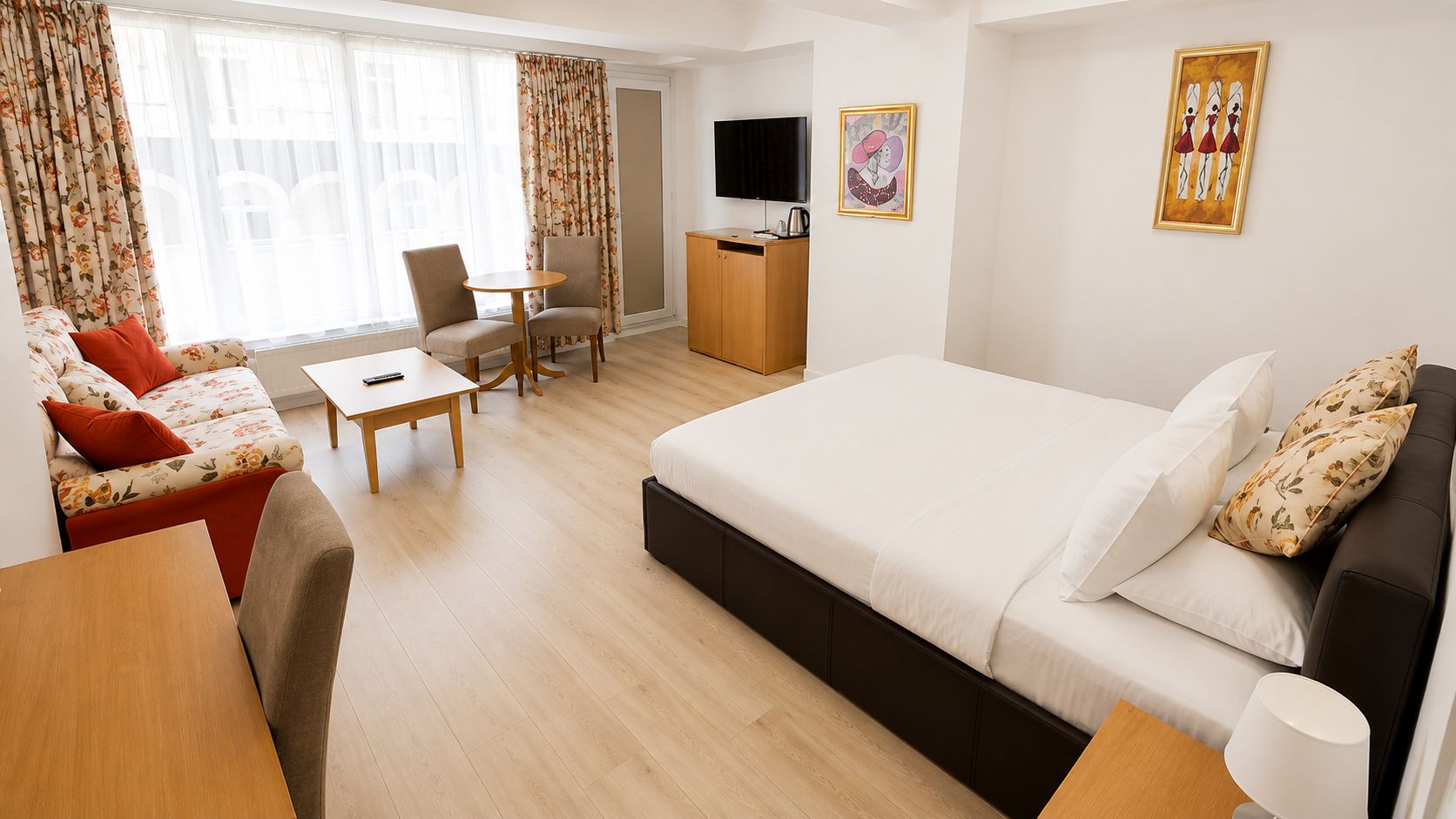 Une chambre d’hôtel équipée d’un lit, d’un canapé, de fauteuils, d’une table, d’un téléviseur et d’œuvres d’art accrochées aux murs.