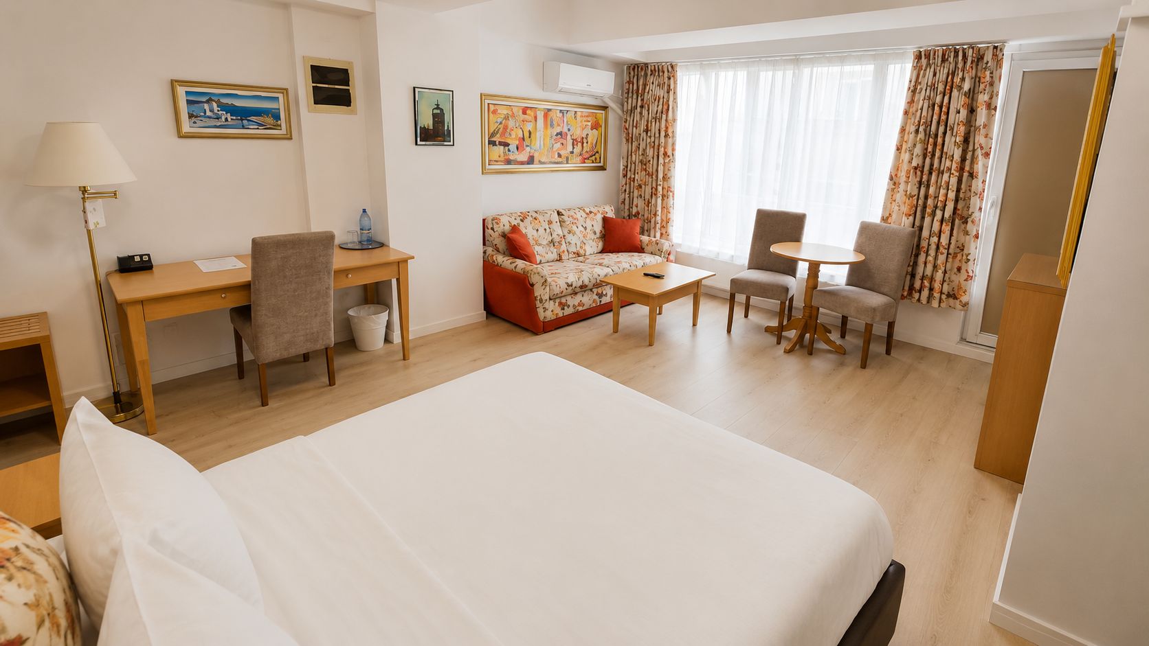 A hotel room with a large bed, a desk, a sofa, a small table, and a chair.