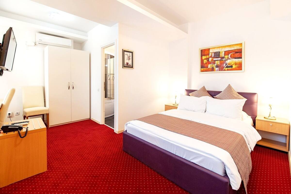 A hotel room with a bed, a desk with a telephone, a shower, and a painting on the wall.