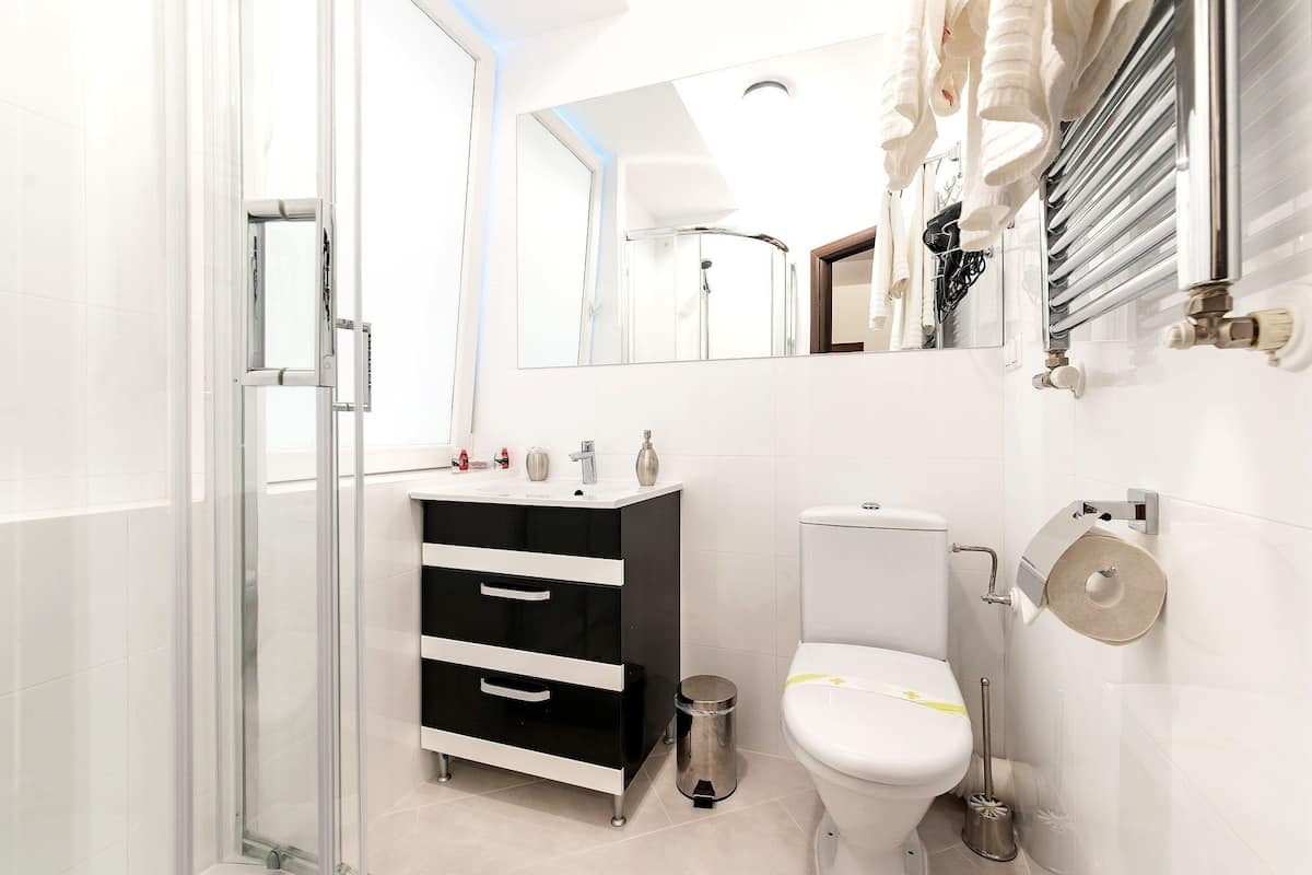 A modern bathroom with a glass shower enclosure, a black and white vanity, a toilet, and a mirror.