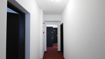 A narrow hallway with white walls and a red carpet. There are doors on both sides, one of which is open.