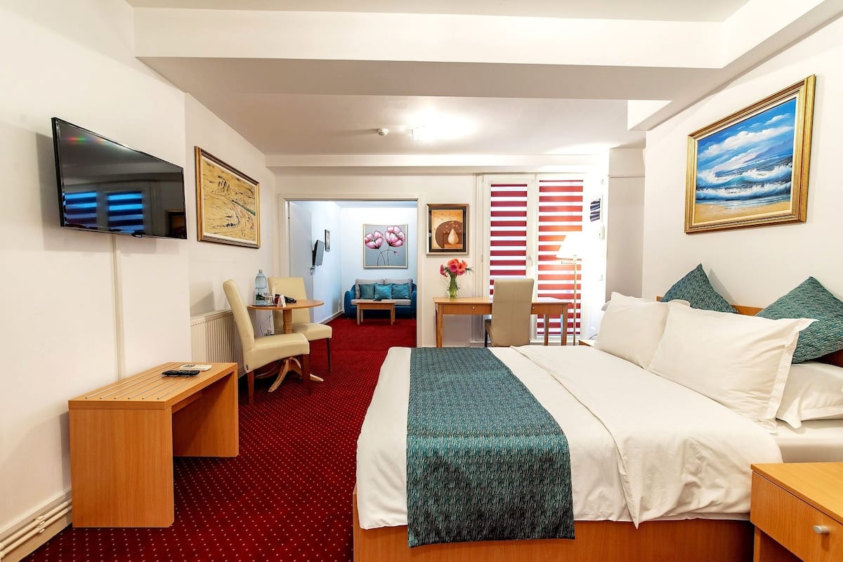 A hotel room with a large bed, a desk, a chair, a TV, and artwork on the walls.