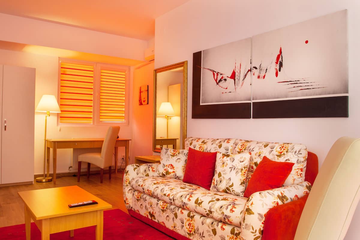 A modern living room with a floral sofa, a wooden coffee table, a desk with a chair, and two lamps.