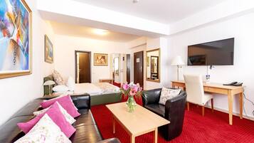 Ein Hotelzimmer mit rotem Teppich, einer Couch, einem Couchtisch, einem Fernseher, einem Schreibtisch und einem Bett.