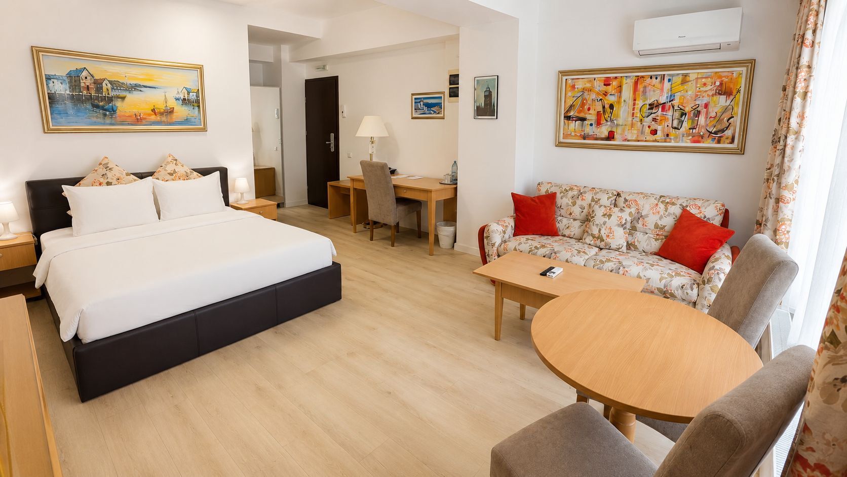 A hotel room with a bed, a sofa, a dining table, and a desk.