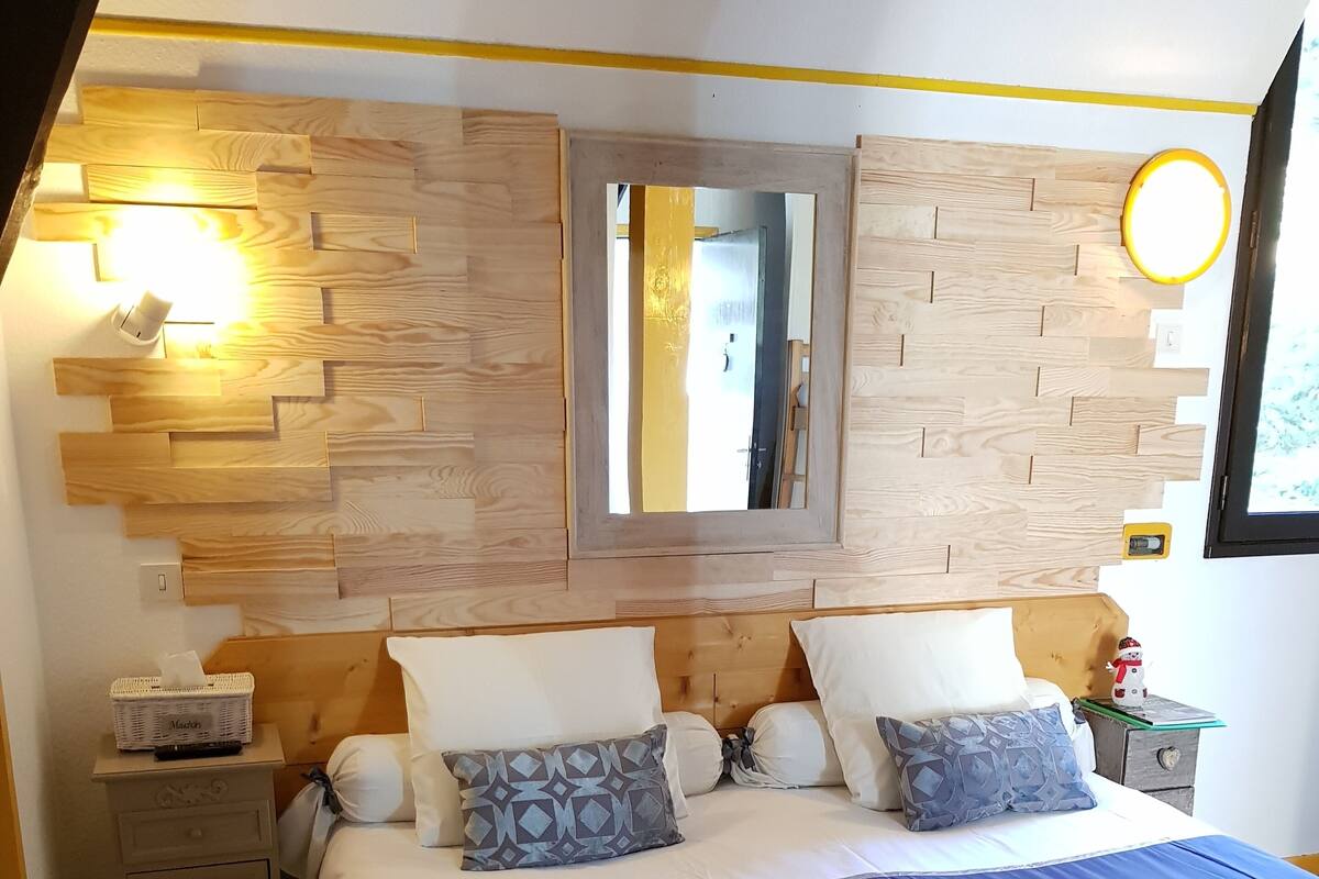 Ein Schlafzimmer mit einem hölzernen Kopfteil, einem großen Spiegel und einem Nachttisch mit Lampe.