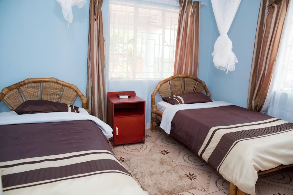 Quarto com duas camas, uma mesa de cabeceira vermelha e uma janela com cortinas.
