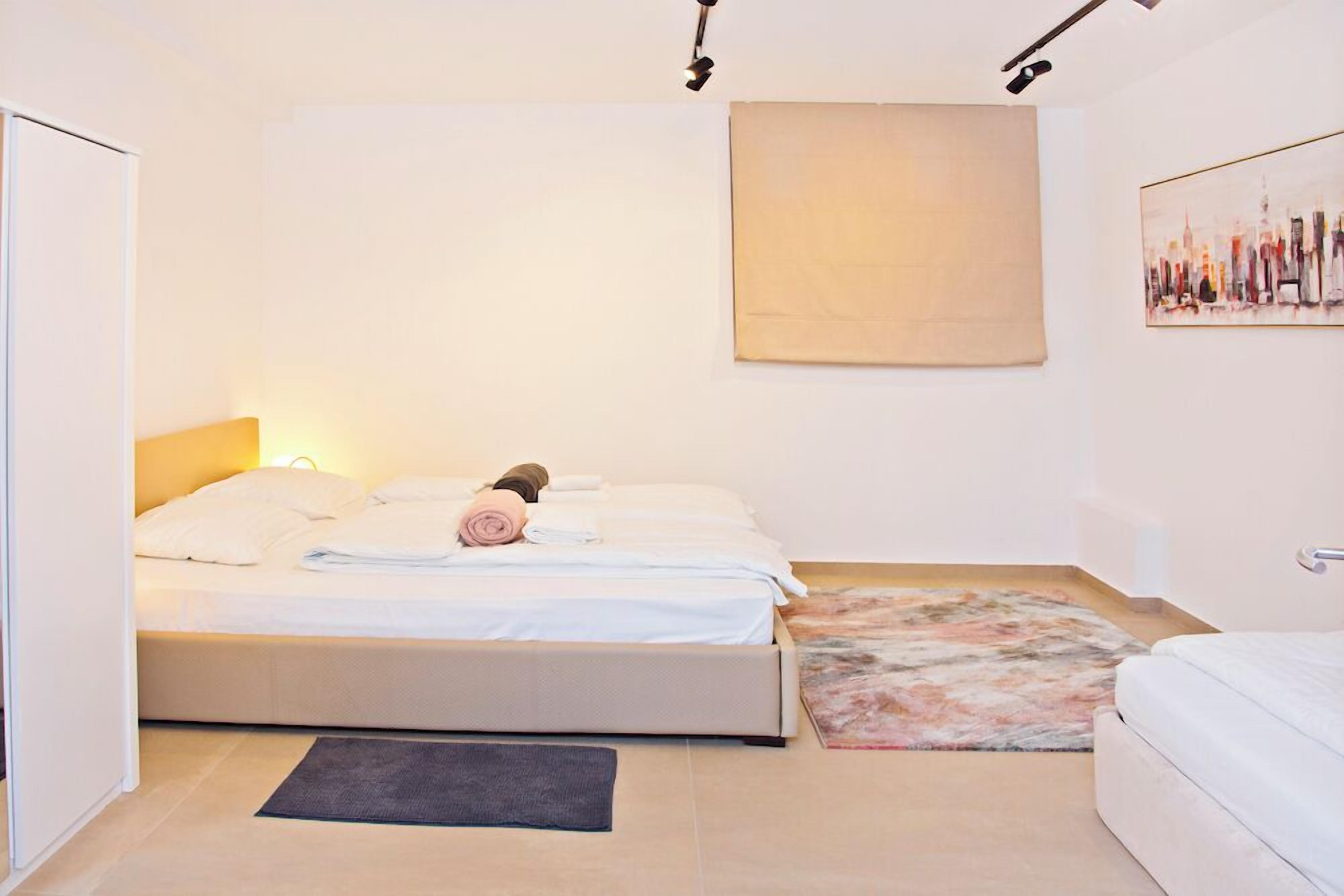 Un dormitorio con una cama, una alfombra pequeña, un cuadro en la pared y una puerta.