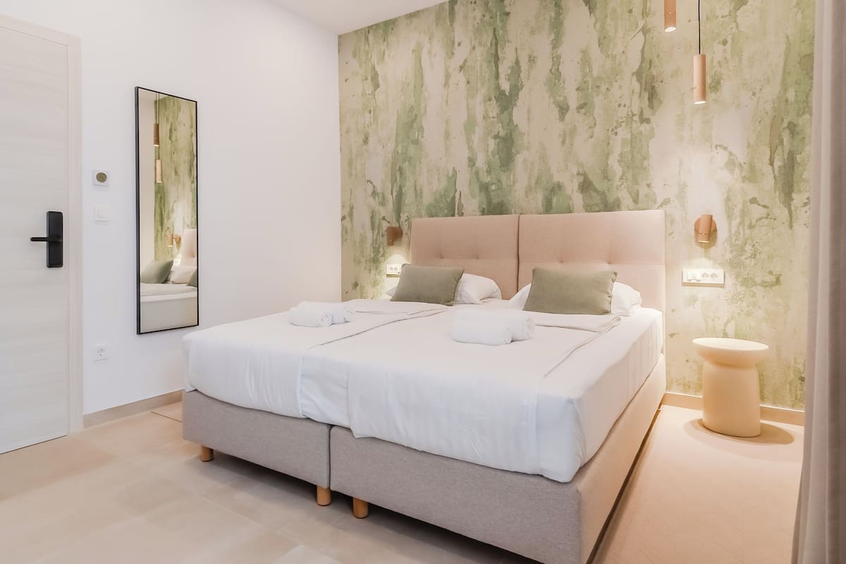 A modern bedroom with a large bed, a bedside table, and a wall-mounted mirror.