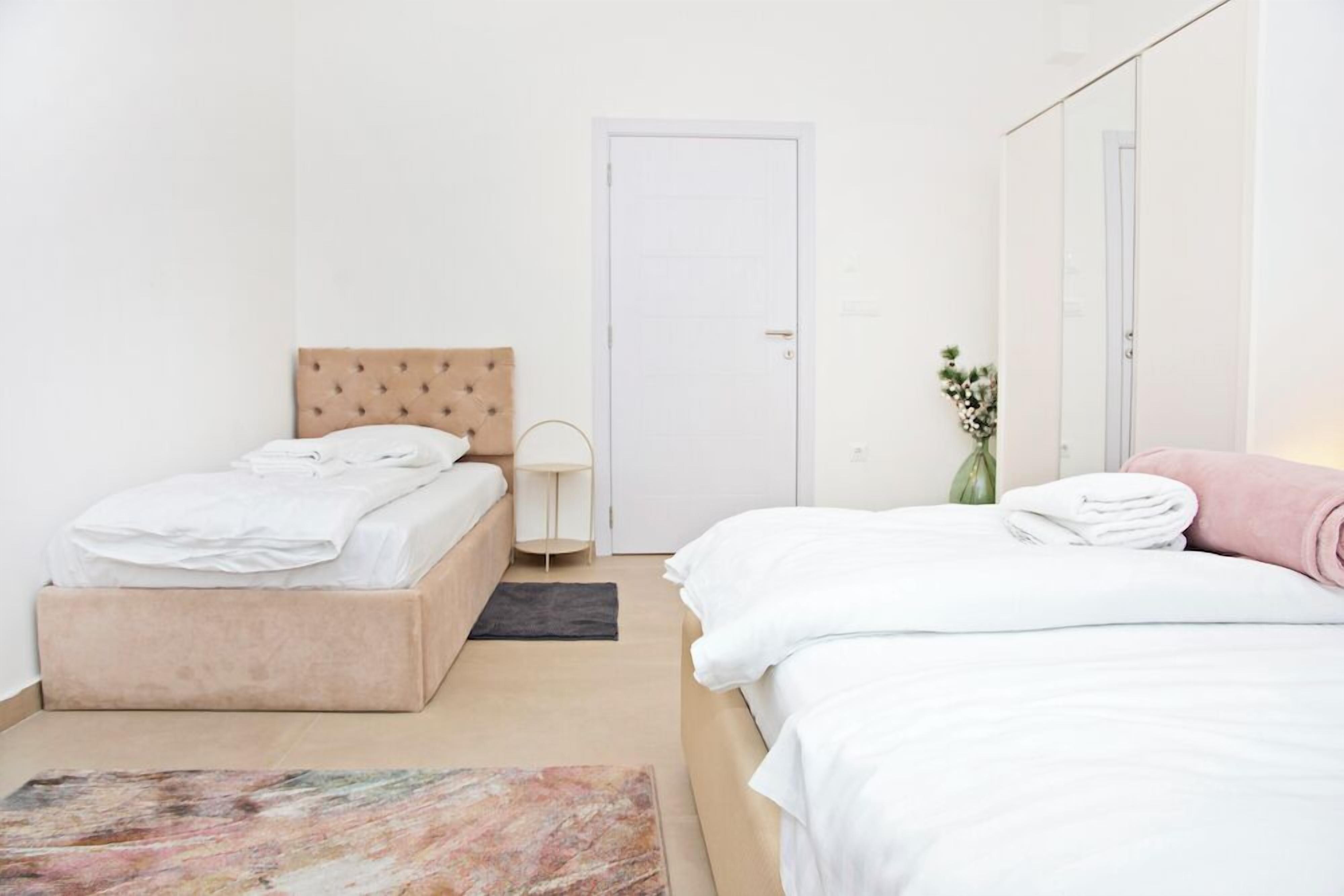 Un dormitorio con cama, una mesita de noche, una lámpara, una puerta y un pequeño florero con flores.
