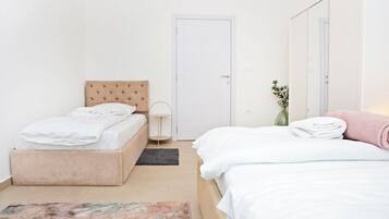 Un dormitorio con cama, una mesita de noche, una lámpara, una puerta y un pequeño florero con flores.