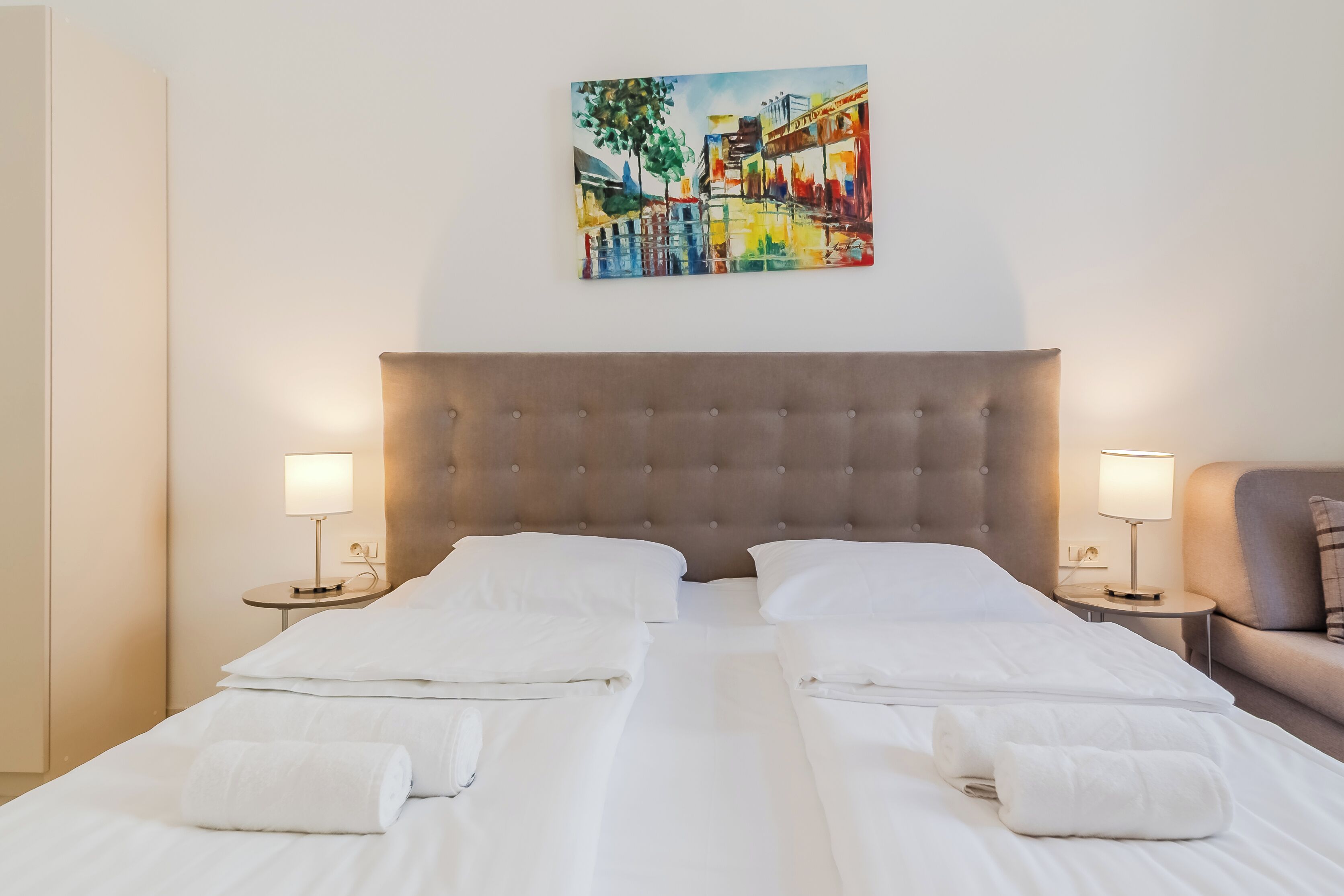 A hotel room with a large bed, two bedside tables with lamps, a headboard, and a painting on the wall.