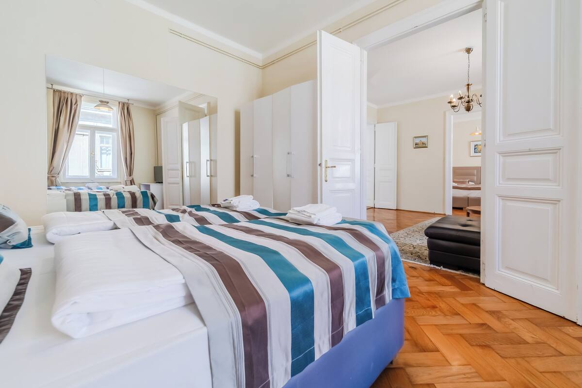 A hotel room with a large bed, a wardrobe, a bathroom, and a hallway leading to another room.