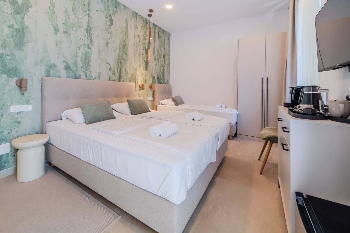 A hotel room with two beds, a small seating area, a TV, and a kitchenette.