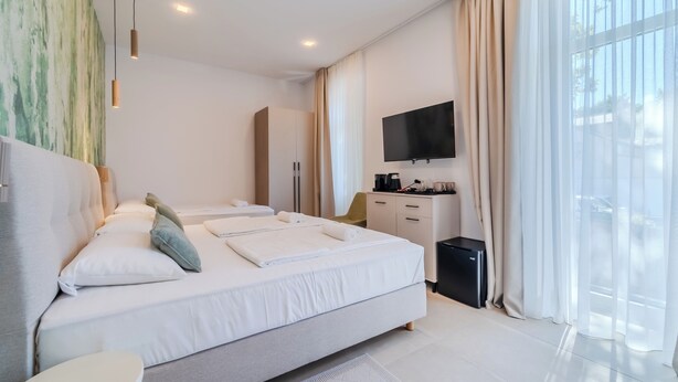 A modern hotel room with a large bed, a bedside table, a flat-screen TV, and a view of the outdoors. - Flowers Premium Apartments & Rooms (Zagreb)