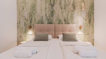 A double bed with a tufted headboard, two bedside tables with wall-mounted lamps, and neatly folded towels on the bed.