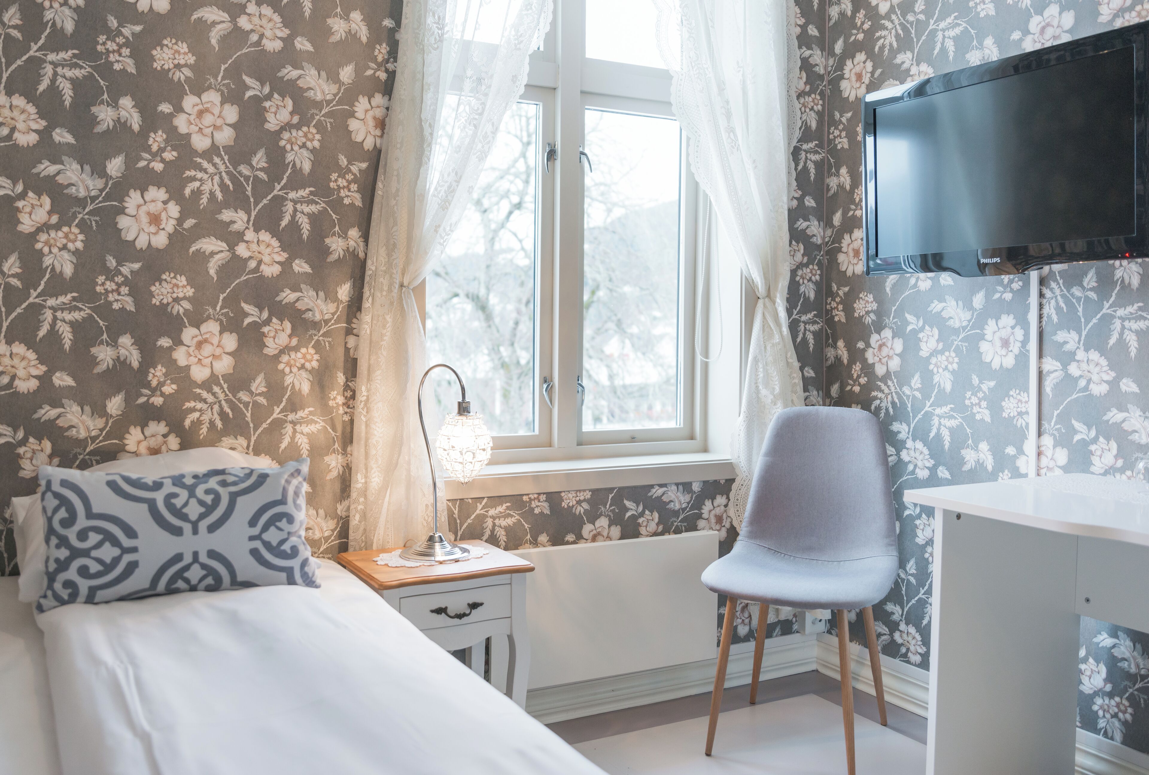 A bedroom with a bed, a chair, a desk, a lamp, and a TV.