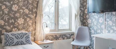 A bedroom with a bed, a chair, a desk, a lamp, and a TV.