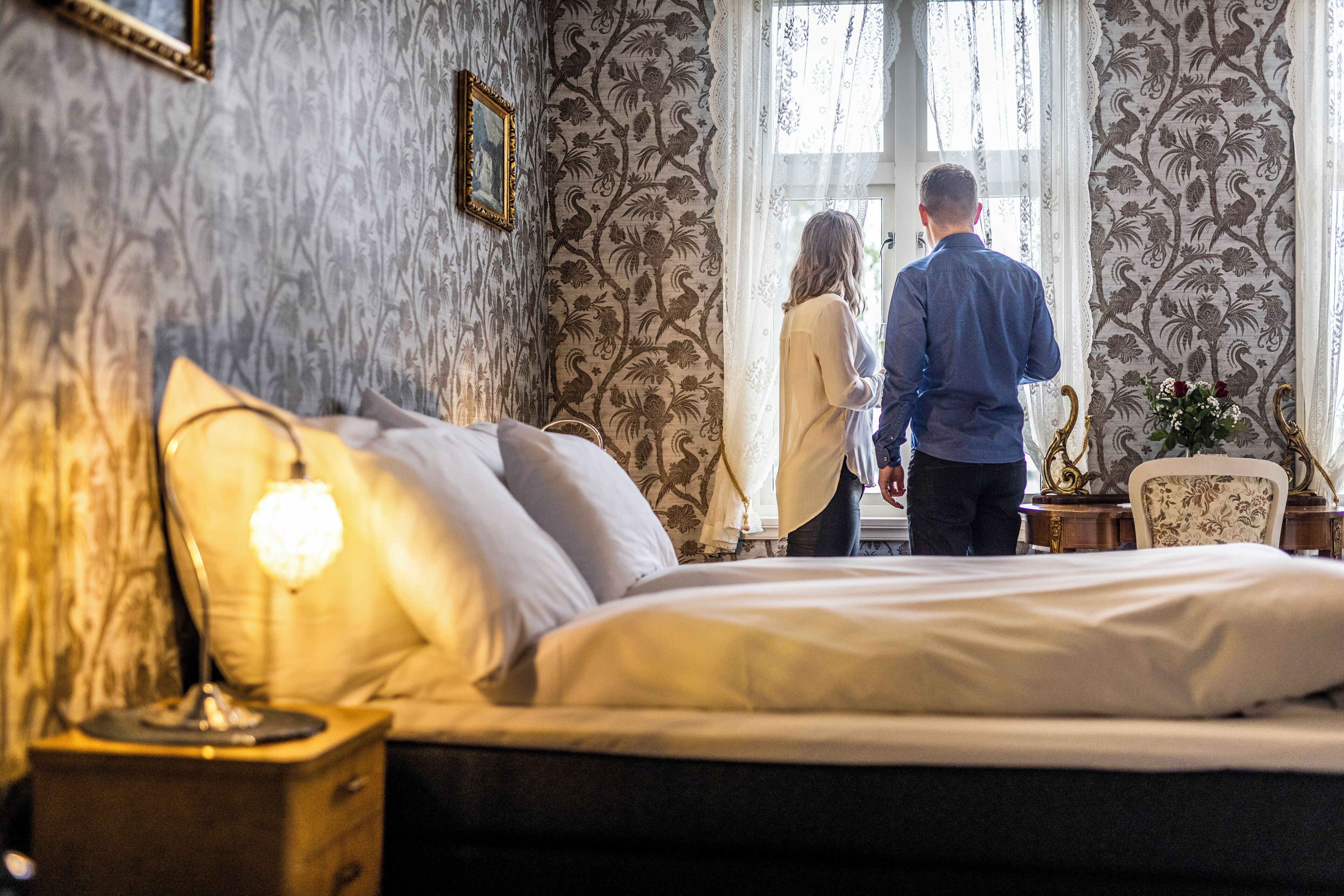 A bedroom with a bed, a nightstand, a lamp, and a window with curtains.