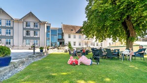 Ein Hotelinnenhof mit Außenbestuhlung, einer Steinmauer und einem großen Baum, der Schatten spendet.