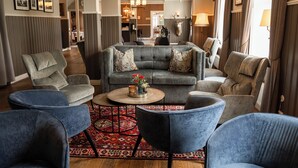 Ein geräumiges Wohnzimmer mit einem grauen Sofa, blauen Sesseln und einem gemusterten Teppich.