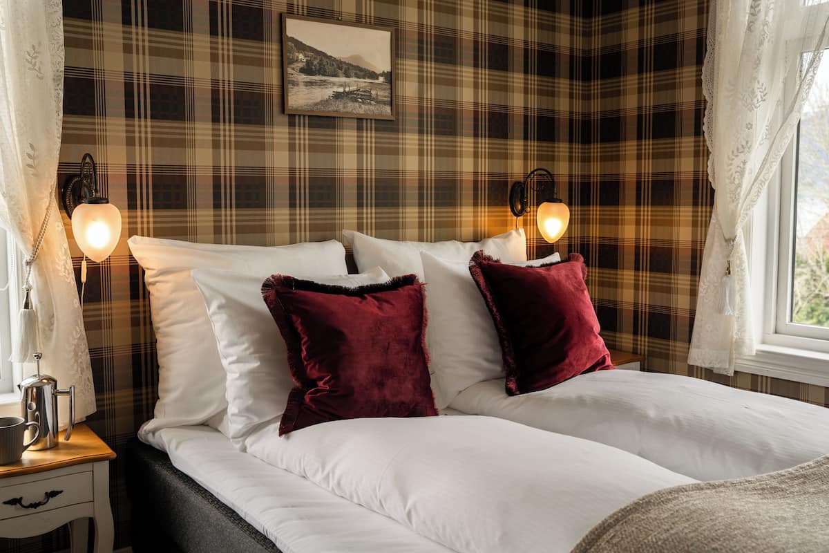 A bed with white and red pillows, a plaid-patterned wall, and two wall-mounted lamps.