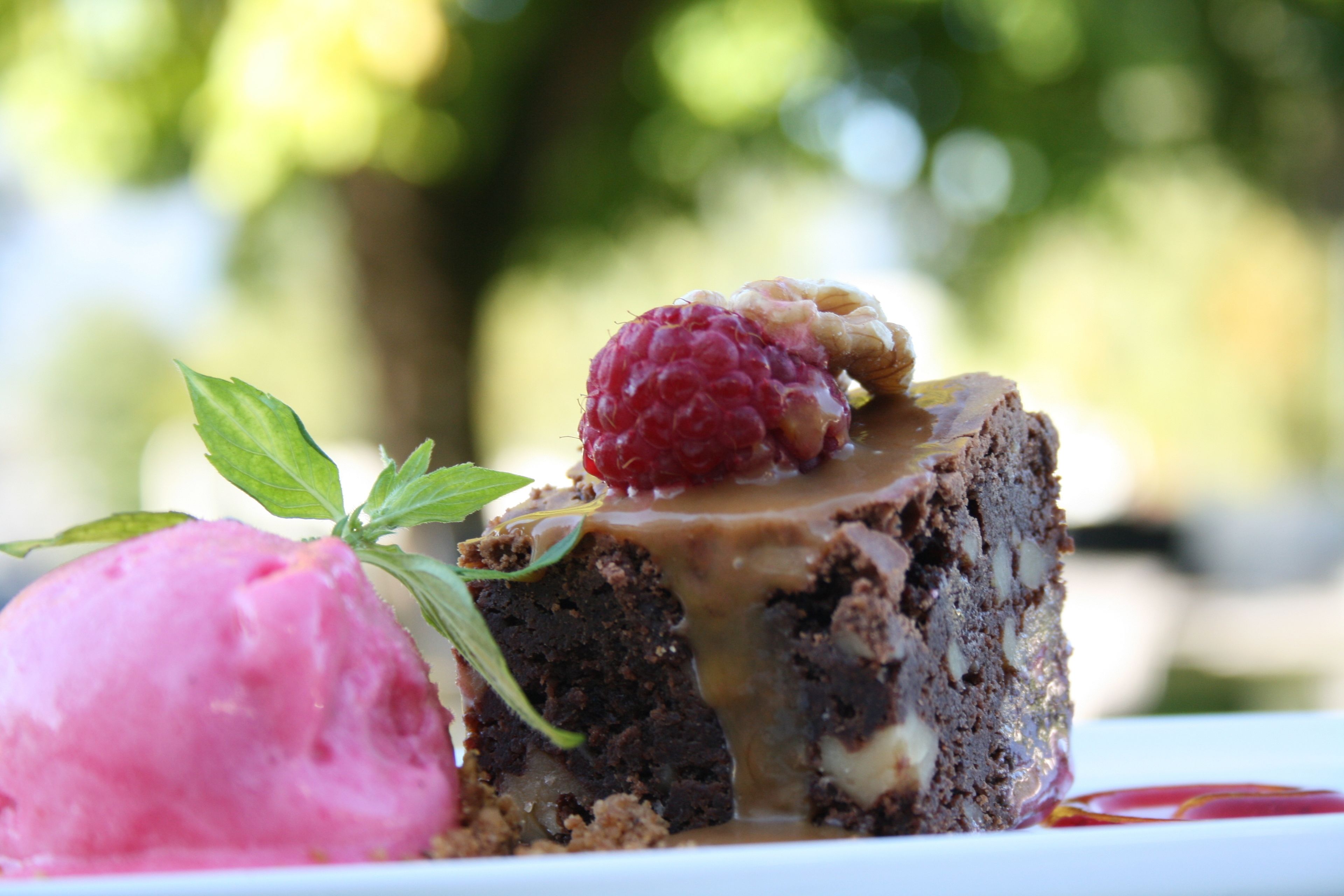 Dessert med en hindbær ovenpå, en scoop lyserød is ved siden af, og et lag sauce henover.