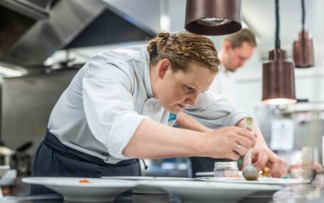 A chef preparing food in a modern kitchen with stainless steel appliances and pendant lighting.