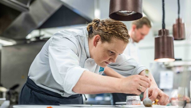 Ein Koch bereitet Essen in einer modernen Küche mit Edelstahlgeräten und Pendelleuchten zu.