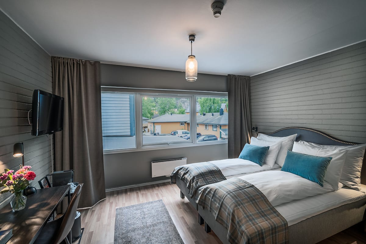 A bedroom with a bed, a TV, a window, and a view of the outside.