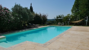 Une piscine rectangulaire dont les bords sont recouverts de carreaux, entourée d’un patio aménagé avec des chaises longues et un hamac.