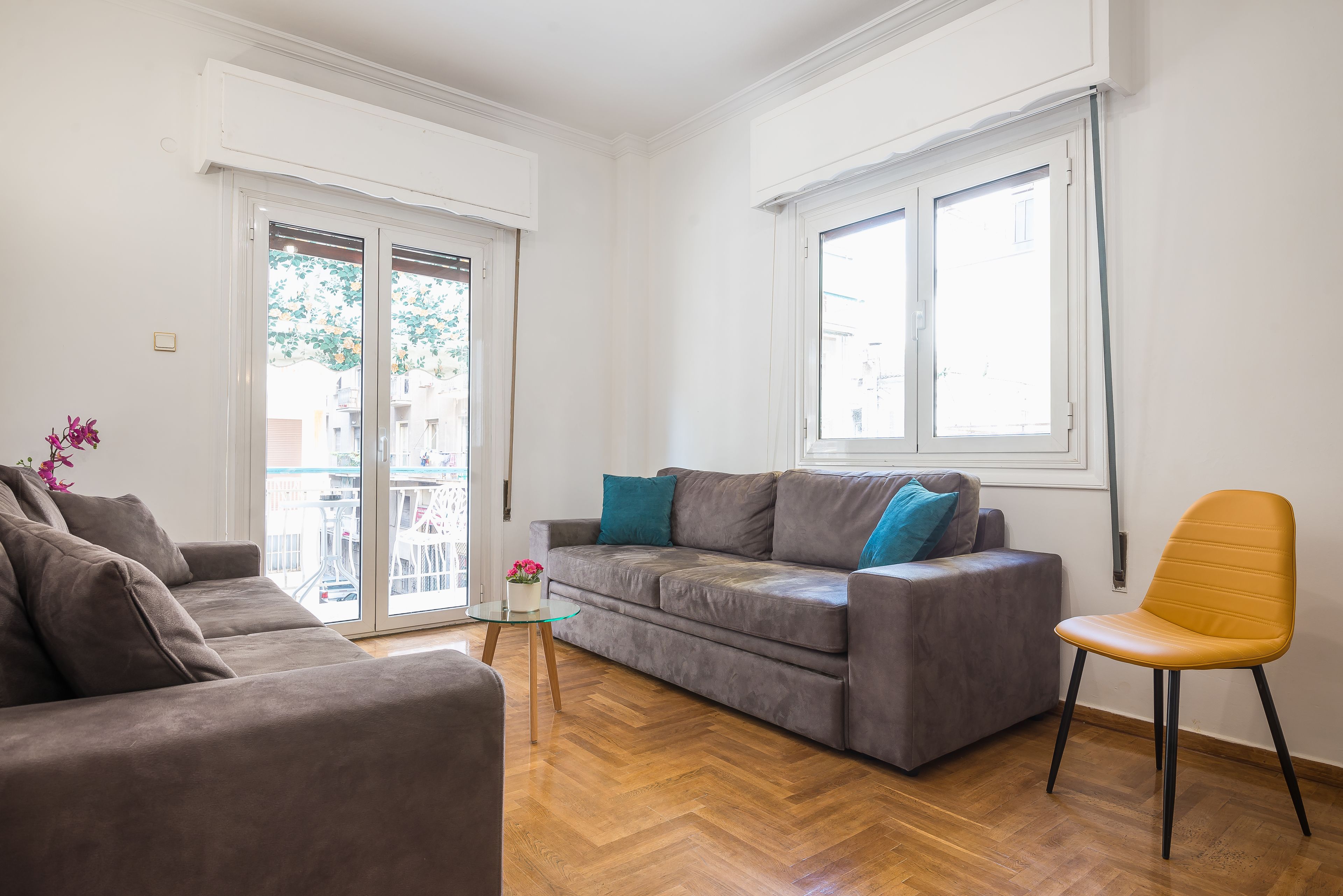 Un salon moderne avec un canapé gris, un fauteuil jaune et une table basse en verre.